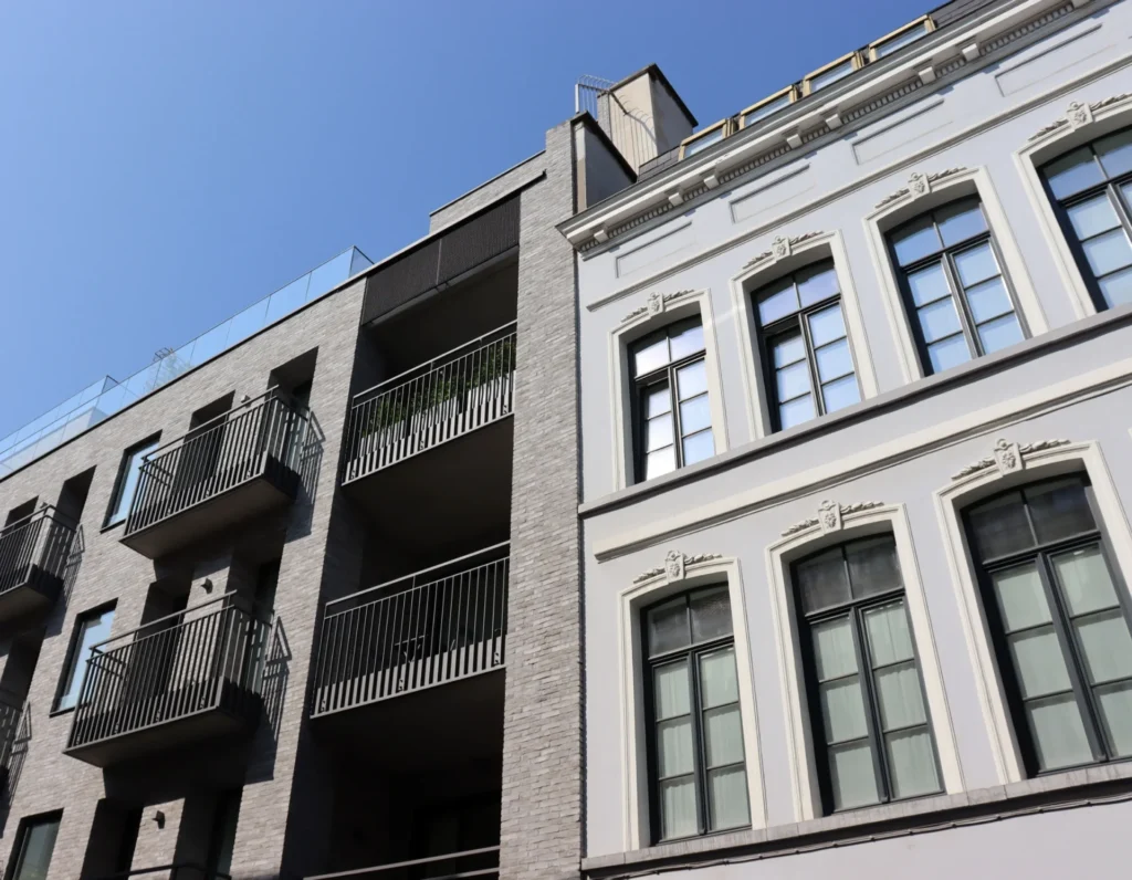 Zwei benachbarte Gebäude: Ein Altbau und ein Neubau, die nebeneinander stehen und den Kontrast zwischen traditioneller und moderner Architektur zeigen. Der Altbau ist älter und weist klassische Bauelemente auf, während der Neubau modernere Materialien und ein zeitgenössisches Design verwendet.