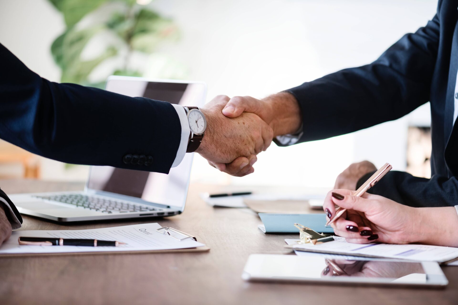Zwei Männer in Anzügen schütteln sich die Hand, was eine geschäftliche Vereinbarung oder Zusammenarbeit symbolisiert. Die Szene vermittelt Professionalität und Vertrauen.