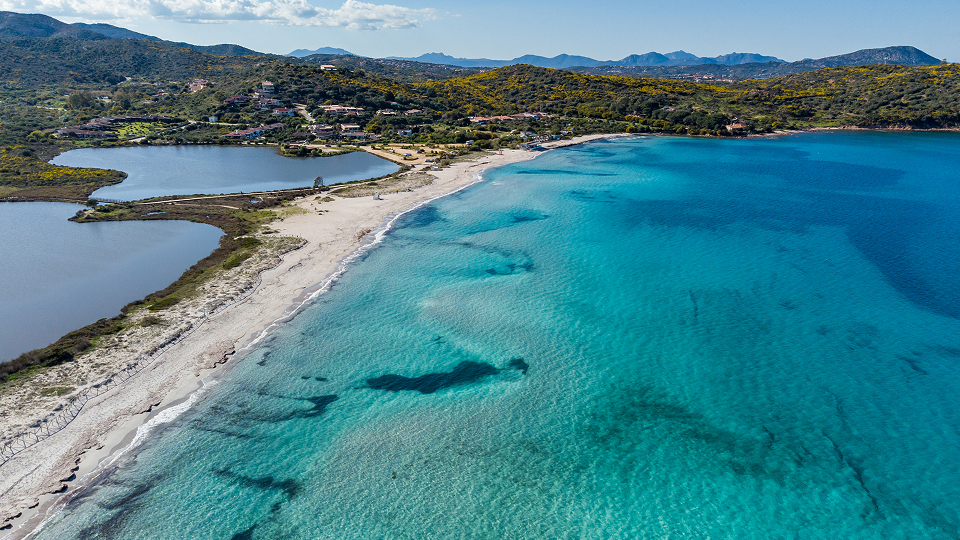 Panoramablick auf den Strand Porto Taverna in Nord-Sardinien mit türkisblauem Meer, feinem Sandstrand und Blick auf die Insel Tavolara im Hintergrund.